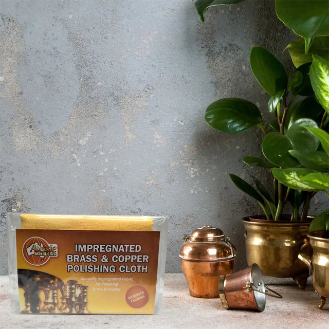 Brass and copper polishing cloth packaging with brass and copper items on a stone surface.