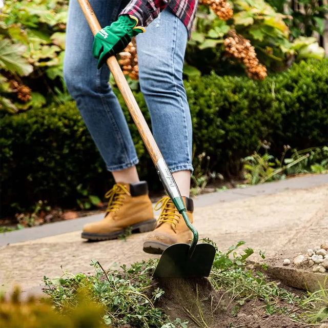 Person gardening with a hoe and green gloves in a garden setting