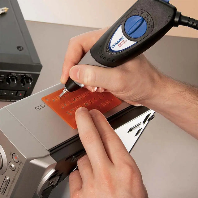 Person using a Dremel tool on a red cutting mat with a machine in the background.