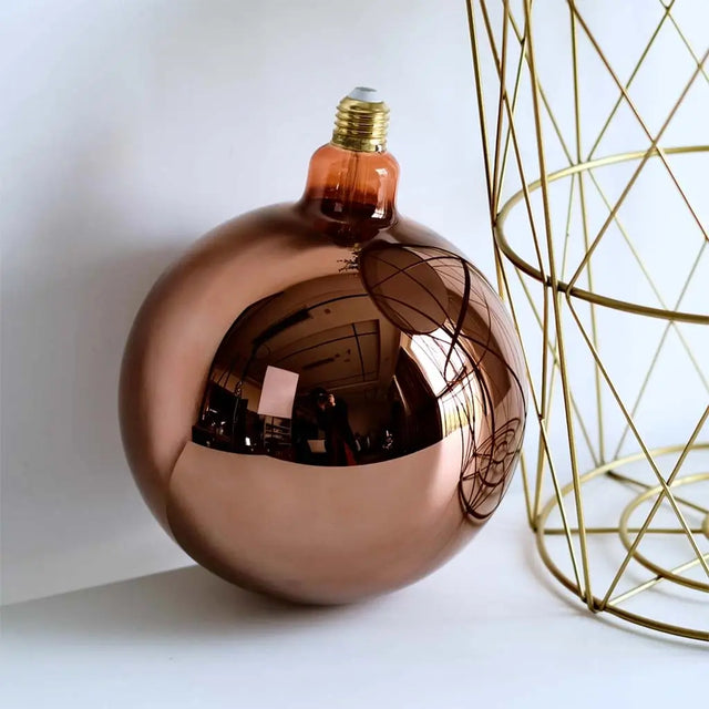 Copper-colored spherical object with a light bulb inside, next to a gold geometric wireframe sculpture.