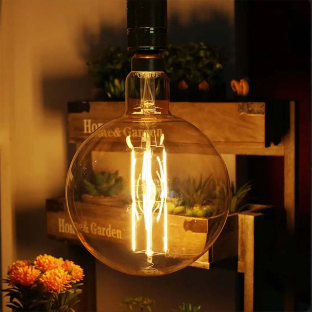 Vintage-style light bulb in a decorative setting with plants and wooden boxes.