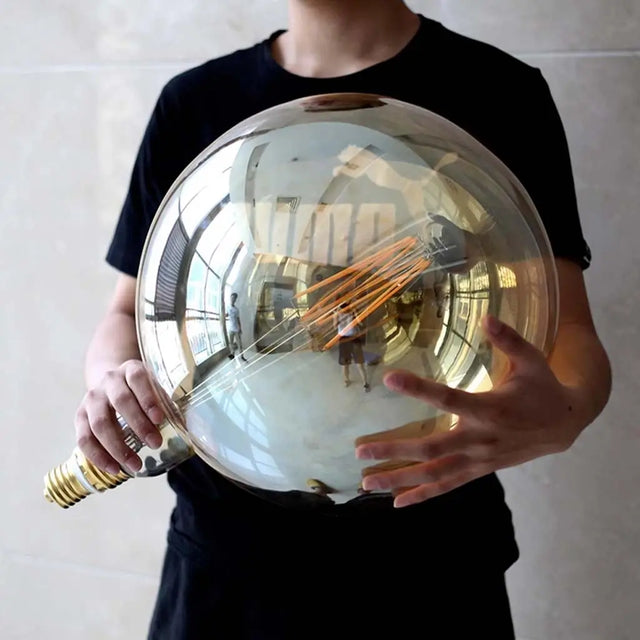 Person holding a large reflective metallic sphere with a blurred indoor background