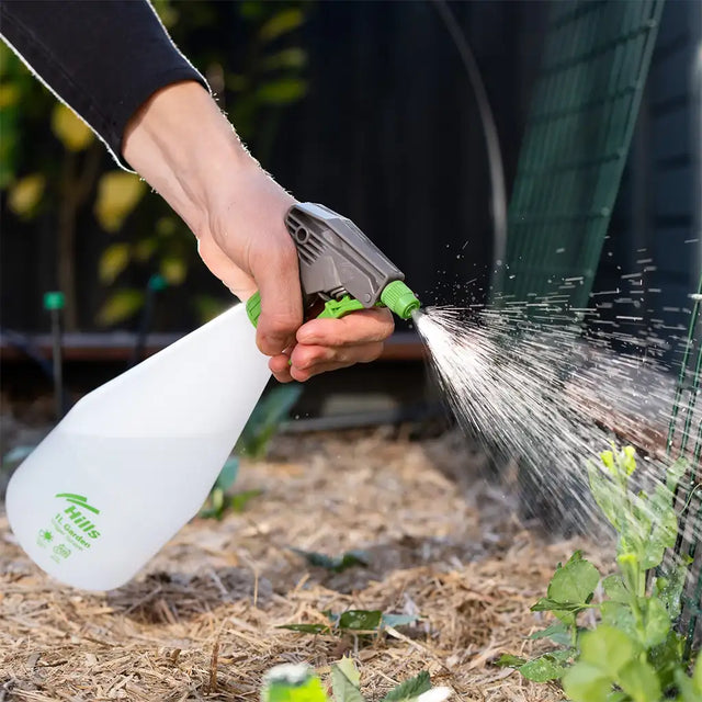 Person using a spray bottle to water plants in a garden setting