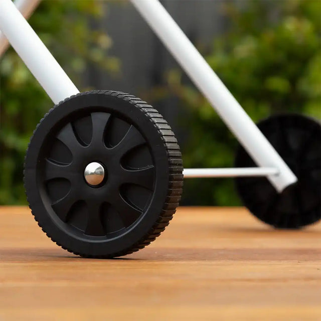Close-up of a black wheel on a wooden surface with blurred greenery in the background