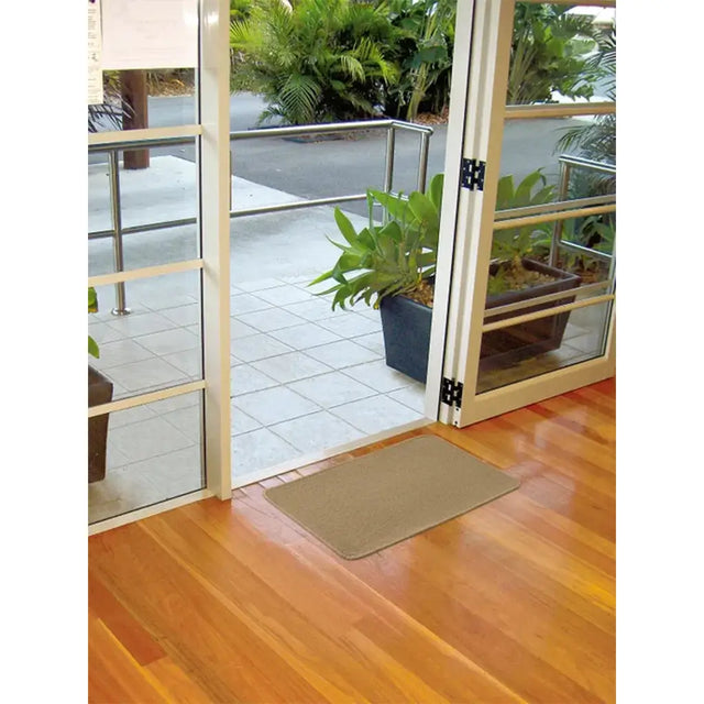 Brown doormat on a wooden floor in front of glass doors leading to a patio with plants.