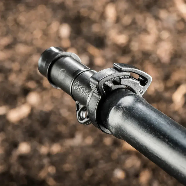 Close-up of a irrigation pipe fitting with 'pope' branding against a blurred natural background.