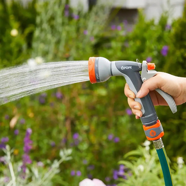 Person using a garden hose with a nozzle to water plants in a garden.