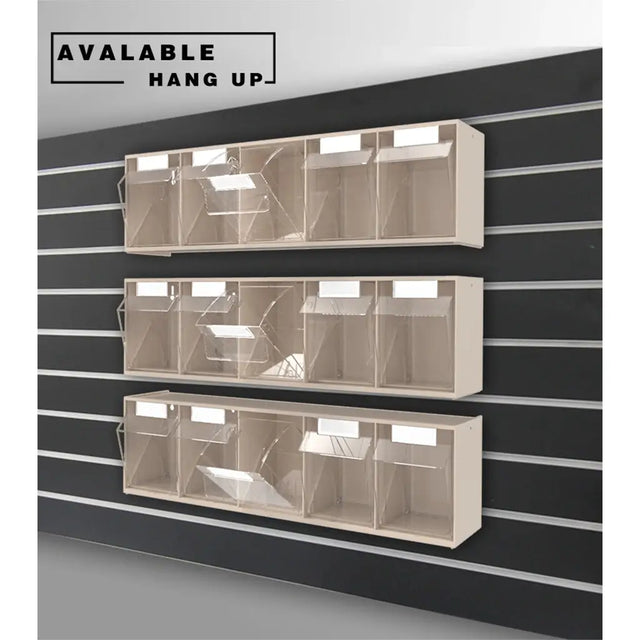 Three beige wall-mounted display racks with clear plastic bins, shown hanging on a black slatwall. A text label in the top left reads 'AVAILABLE HANG UP'.