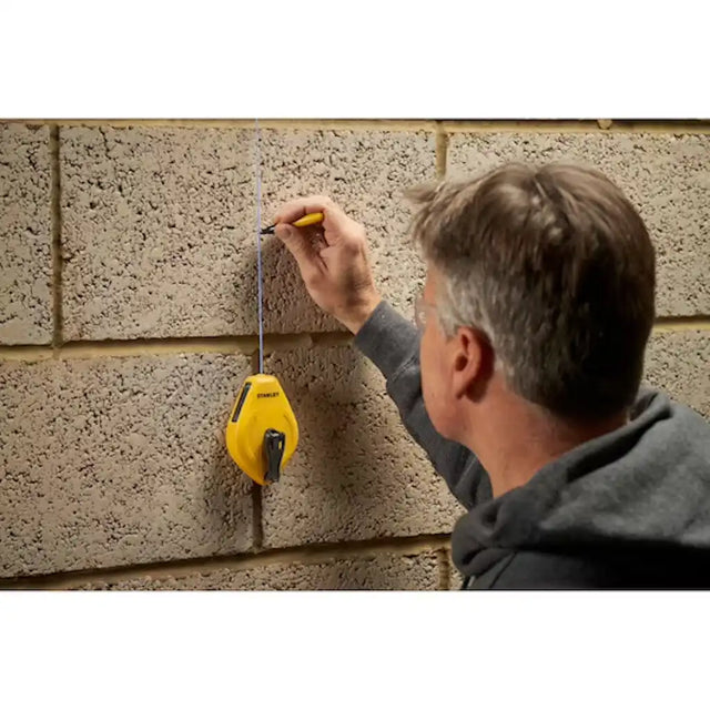 Person using Stanley chalk line reel as a plumb bob against a brick wall