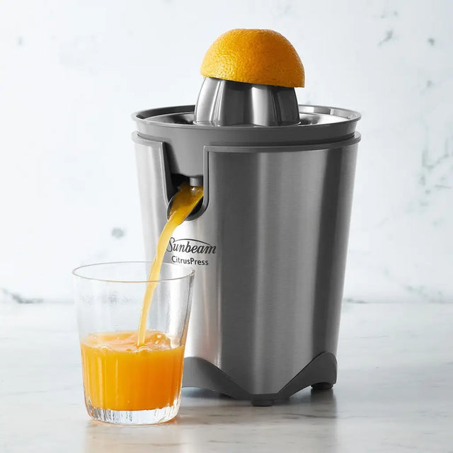 Sunbeam citrus press juicing an orange with juice flowing into a glass on a light background