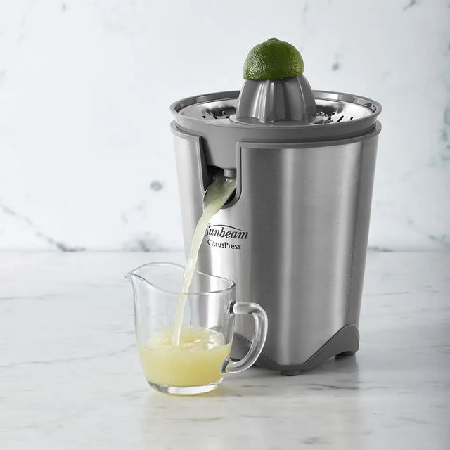 Sunbeam citrus press juicing a lime with juice collected in a glass on a marble surface.