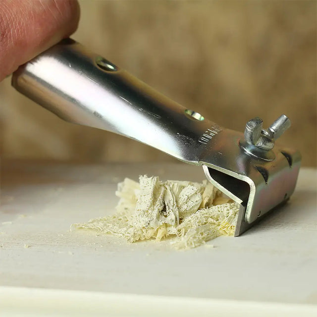 Metallic tool with a piece of cheese being sliced on a wooden surface