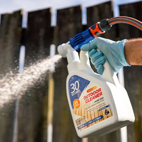 Person using a spray bottle labeled '30 Seconds Outdoor Cleaner' to clean a wooden fence.
