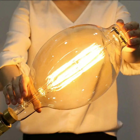 Person holding a large, vintage-style light bulb with a warm glow.