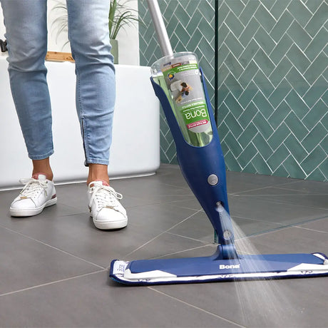 Person using a Bonn floor cleaning device on a tiled floor with a green wall in the background.