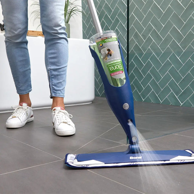 Person using a Bonn floor cleaning device on a tiled floor with a green wall in the background.