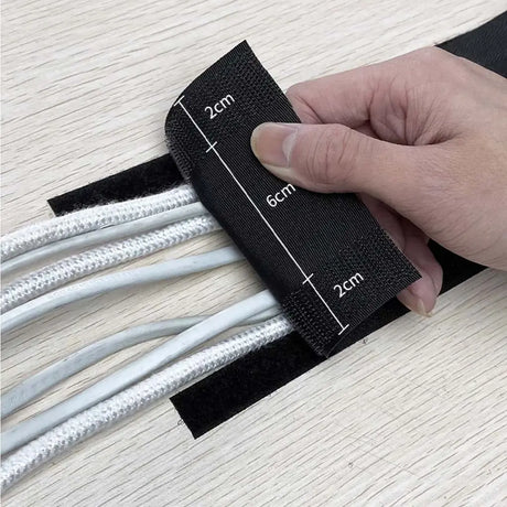 Hand using a black cable management strip with measurements on a light wooden surface.