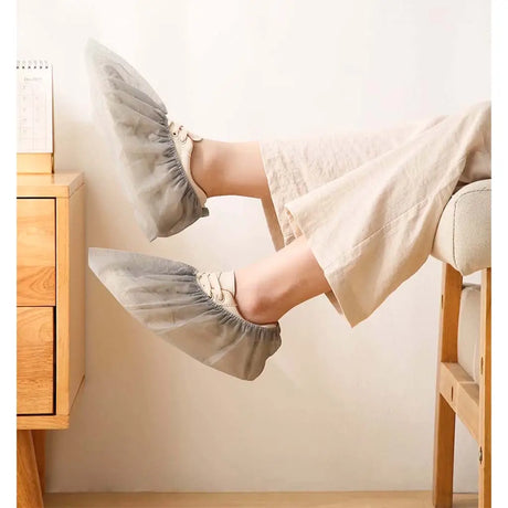 Person wearing gray shoe covers sitting on a chair with a wooden desk and white wall in the background.