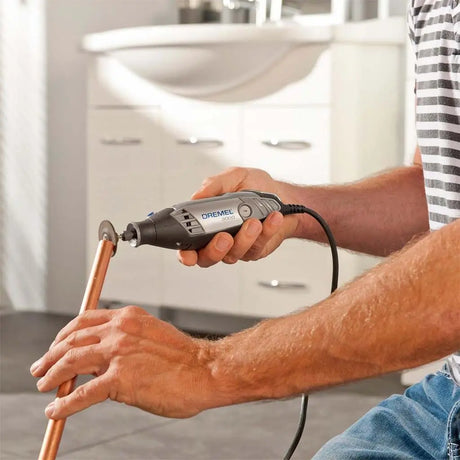 Person using a Dremel tool on a copper pipe in a bathroom setting