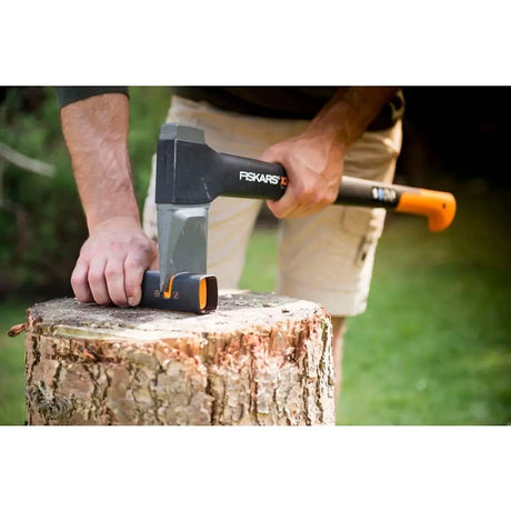 Person using a Fiskars axe on a log with a blurred outdoor background