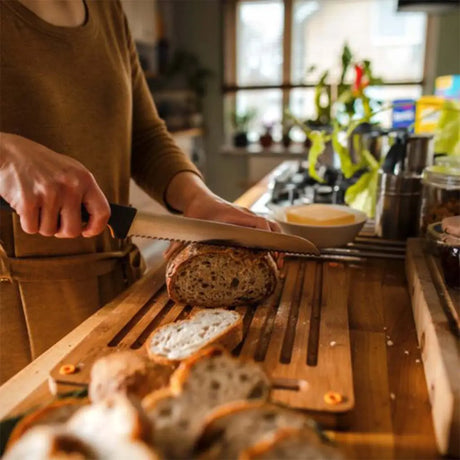 Person slicing bread on a wooden cutting board in a kitchen.
