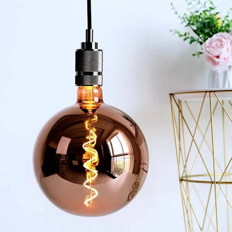 Copper pendant light bulb with decorative interior against a white wall.