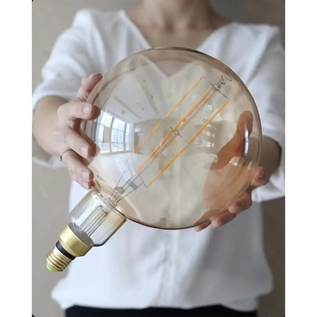 Person holding a large decorative light bulb inside a transparent sphere