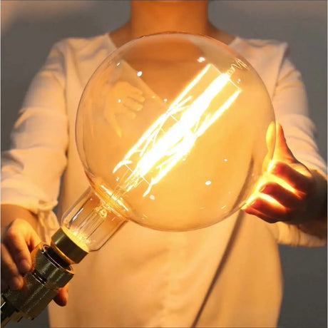 Person holding a large, round, vintage-style light bulb with a warm glow.