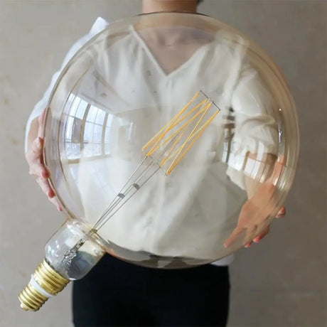 Person holding a large transparent light bulb with visible filament