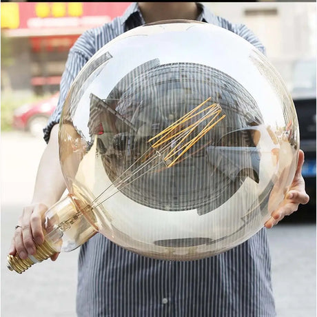 Person holding a large transparent sphere with a light bulb inside, outdoors.