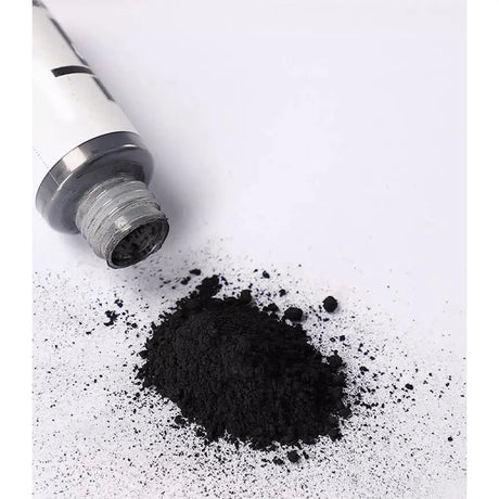 Spilled black powder next to a white and silver cylindrical container on a white background