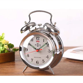 Silver alarm clock with white face on a wooden surface