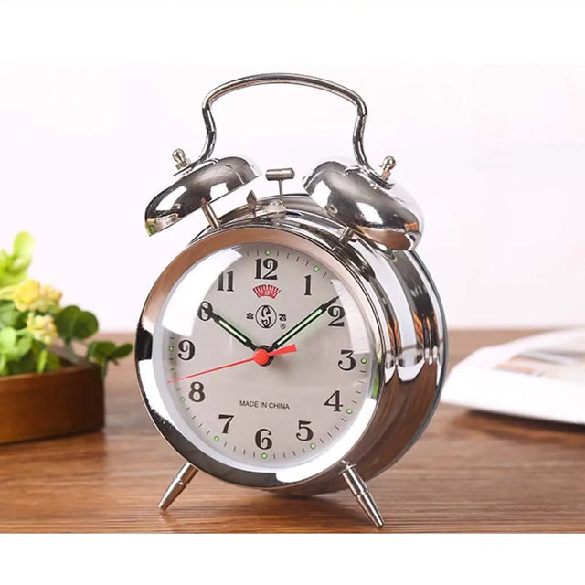 Silver alarm clock with white face on a wooden surface