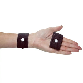 Hand wearing a brown wristband with a small circular hole on a white background