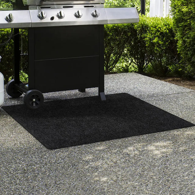 Black grill mat on a concrete surface with a grill in the background