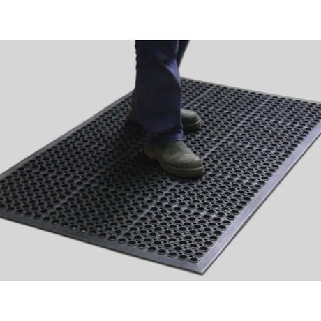 Person stepping onto a textured black mat on a light gray floor.