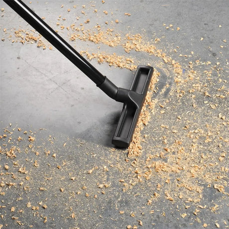 Black vacuum cleaner head cleaning a gray surface with debris.