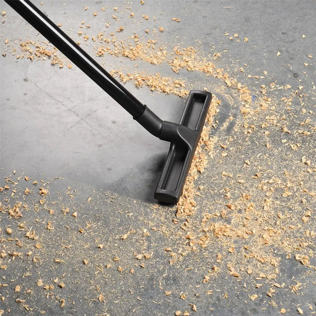 Black vacuum cleaner head cleaning a gray surface with debris.