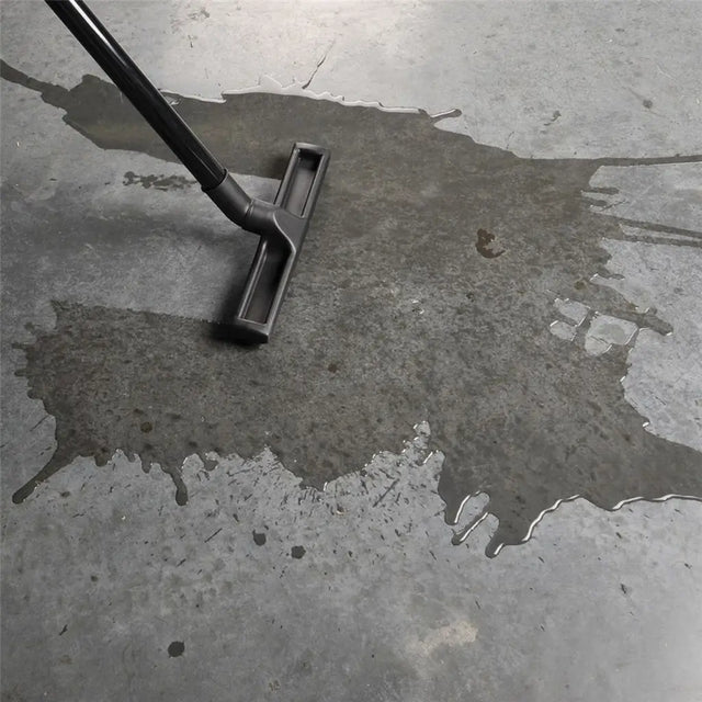 Vacuum cleaner cleaning a wet concrete floor with visible water stains.