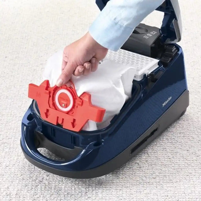Person replacing a filter in a blue vacuum cleaner on a white carpet.