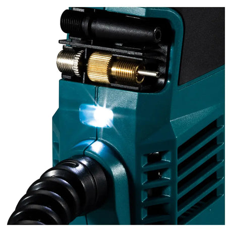 Close-up of a teal welding machine with a black cable, brass adjustment knobs, and a bright white arc light glowing on a white background.