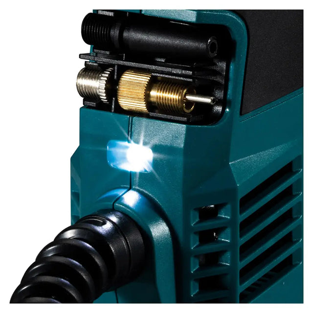 Close-up of a teal welding machine with a black cable, brass adjustment knobs, and a bright white arc light glowing on a white background.