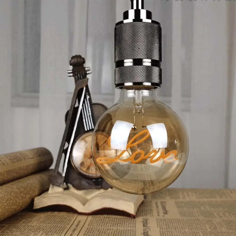 Decorative light bulb with 'Love' on it, placed on a book with a guitar in the background.