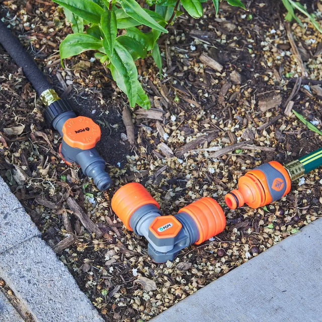 Garden hose with orange connectors on a garden bed
