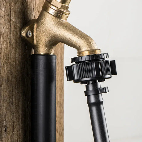 Brass faucet mounted on a wooden wall with a black hose attached.