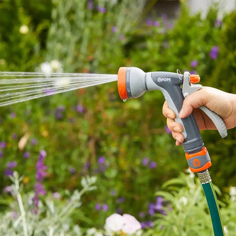 Hand holding a garden hose sprayer with water spraying onto plants