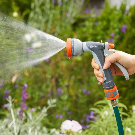 Person using a garden hose with a spray nozzle to water plants in a garden.