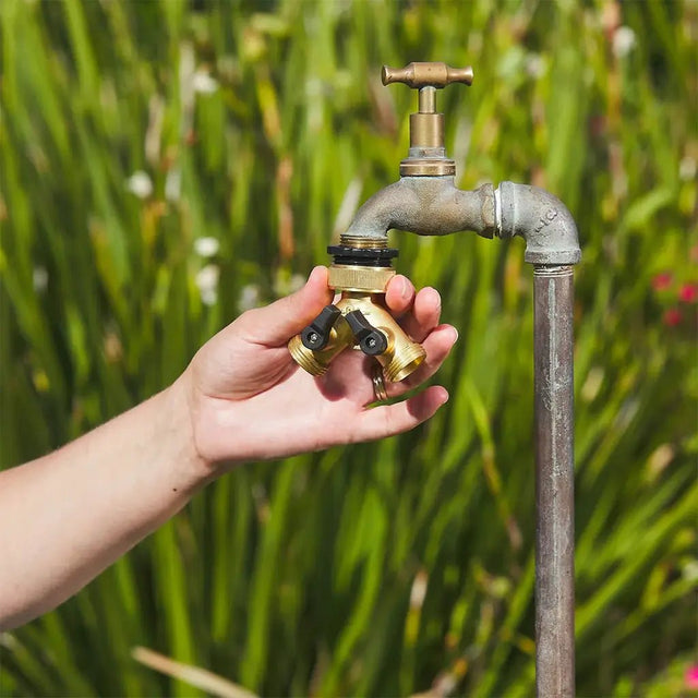 Hand holding a brass garden faucet with a green outdoor background