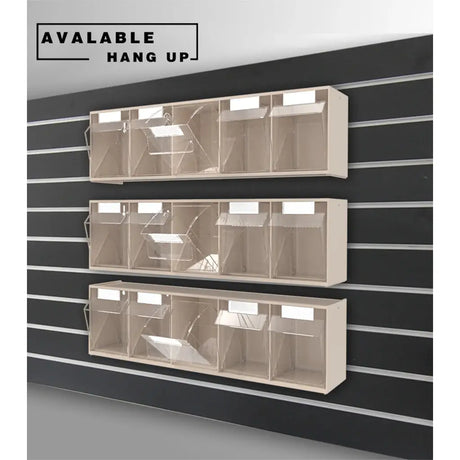 Three beige wall-mounted display racks with clear plastic bins, shown hanging on a black slatwall. A text label in the top left reads 'AVAILABLE HANG UP'.