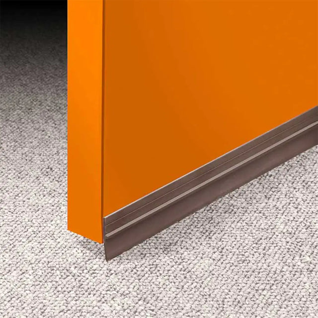 Close-up of an orange door with a threshold ramp on a textured gray floor.
